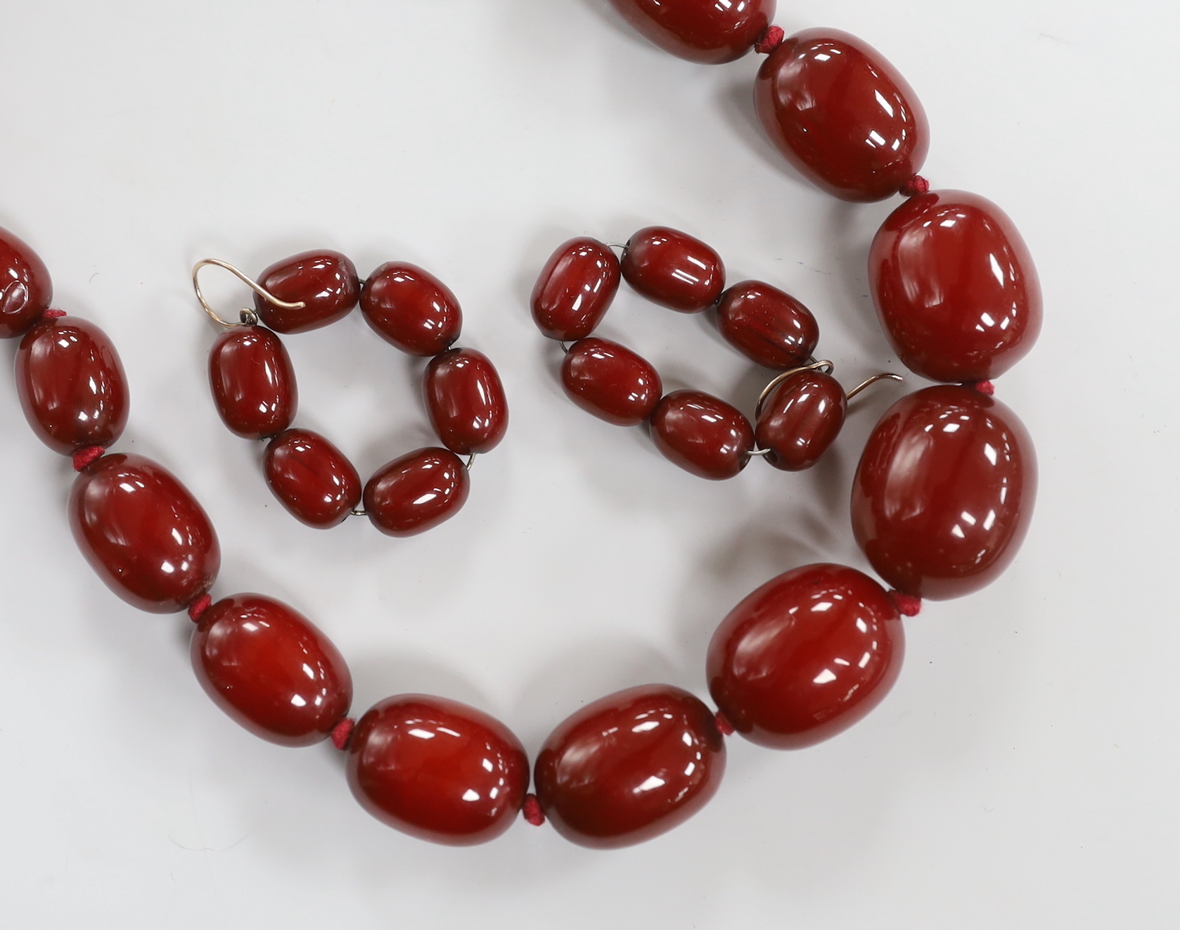 A single strand graduated simulated cherry amber necklace, 64cm and a pair of similar earrings, gross weight 118 grams.